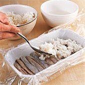 Sushi - Reis wird mit einem Löff el auf dem Fisch verteilt