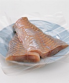 Two fillets of raw fish on plate with transparent foil
