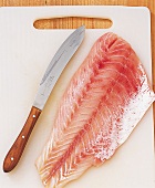 Raw fish with knife on cutting board