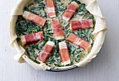 Spinach with ham on dough in baking tray for preparation of quiches, step 3
