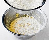 Flour in sieve being put in bowl of batter