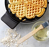 Oatmeal waffles in waffle making machine and bowl of oil with brush