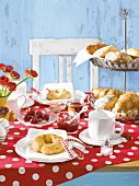 Breakfast table with red and white polka dot table cloth, rolls, croissants, jam and eggs