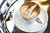 Tasse Kaffee, Milchschaum als Farnblatt verziert, Kakaopulver