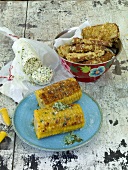 Coconut and sesame tofu in bowl, corn cob with herb and garlic butter on plate