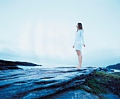 Woman standing on tiptoe on rocks of blue sea and taking breaths peacefully