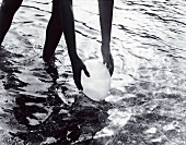 Mensch steht wadentief im Wasser, hebt Ballon auf, schwarzweiß