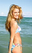 Portrait of pretty blonde woman in colourful bikini standing on beach in Miami, smiling