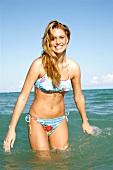 Portrait of happy blonde woman in colourful bikini standing on beach in Miami, smiling