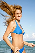 Portrait of happy blonde woman in blue bikini jogging on the beach in Miami, smiling