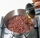 Veal fond being poured on onions in pan