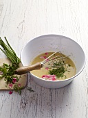 Salad dressing with herbs and flower in bowl with whisk
