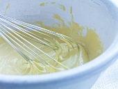 Close-up of oil and egg being whisked in bowl for preparation of cauliflower salad, step 4