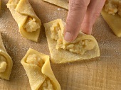 Close-up of hand rolling stuffed biscuits in pasta triangles shape, step 4