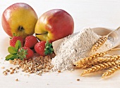 Close-up of apples, strawberries, scoop of flour and grains on white background