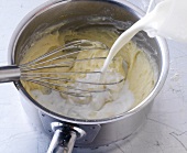 Whisking milk being poured in saucepan for preparation of bechamel sauce, step 2