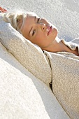 Blonde Frau liegt entspannt im Sand, nachdenklicher Blick