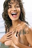 A muddy laughing woman with brown hair stands in water