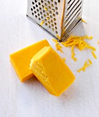 Two pieces of cheddar cheese and grater