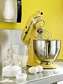 Yellow food processor with blender, mixing bowl, eggs, milk and flour on kitchen stand