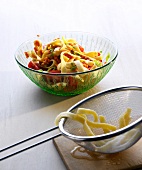 Noodle salad with red coconut lenses in bowl beside strainer