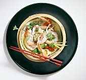 Steamed shrimp with vegetables and ginger slices on plate with chopsticks