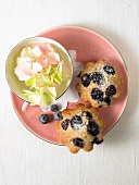 2 kleine Blaubeer-Nuss-Küchlein auf rosa Teller, Tasse mit Blüten