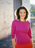 Portrait of pretty woman with dark hair wearing pink top, smiling