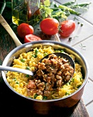 Chicken liver stew with rice and peas in saucepan with tomatoes on table