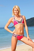 Portrait of attractive blonde woman wearing sports bikini, standing on beach and smiling
