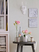 Roses in jug, cup and bottle on wooden stool against white wall