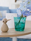 Blaue Blume im grünen Glas auf einem Tisch, daneben eine Holzente