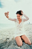 Frau kniet am Strand und schreit wütend