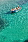 Menschen fahren in einem Boot durchs türkise Wasser, Italien.