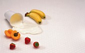 An arrangement of fruit and a spilt yoghurt pot