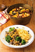 Pot of deer stew and plate of venison ragout with tagliatelle on wooden table