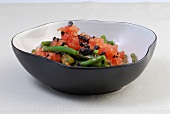 Bowl of bean salad with tomatoes and olives on white background