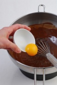 Egg yolk being added in melted chocolate in pan, step 3