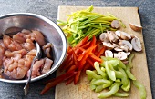 Marinated meat in bowl beside chopped mushrooms, peppers and vegetables on cutting board