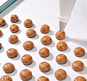 Splash balls being piped from piping bag on baking paper