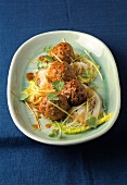 Four meatballs with noodles and cabbage on plate
