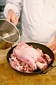 Chef pouring water over veal shank and meat piece in pan