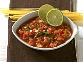 Bowl of tomato and lime sauce with raw spaghetti on napkin