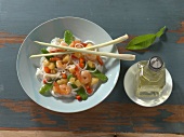 Rice noodles with vegetables and shrimps on plate with chopsticks and oil bottle