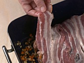 Leg of venison being covered with bacon in baking dish, step 3
