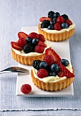 Three lemon berry tartlets with strawberries and blueberries on plate