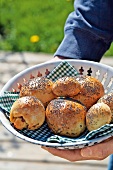 Close-up of man's hands holding bread basket with poppy seed roll 