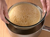 Bowl of mixture being placed in saucepan with water while preparing sabayon sauce, step 2