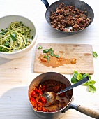 Noodles with arugula and tomatoes in bowl and ground beef in pan