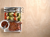 Two fish skewers, two vegetable skewers, marinade and neck chop in serving dish